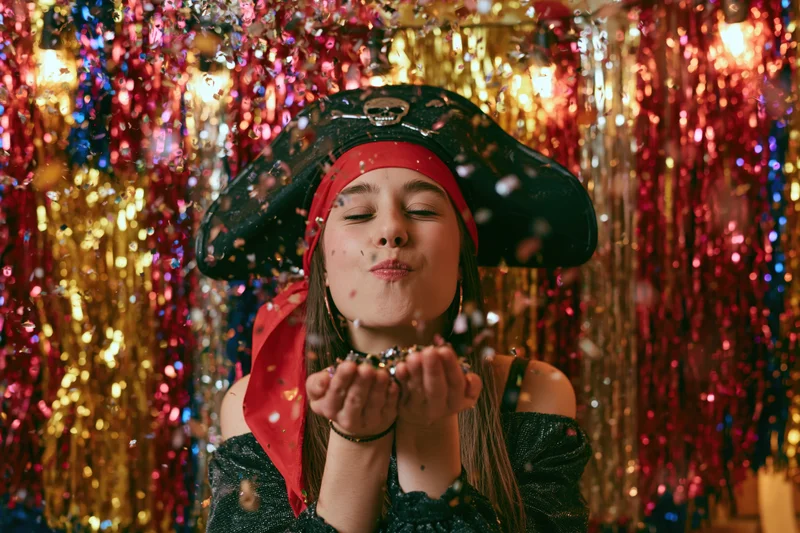 Young woman in pirate costume blowing confetti against a glittering tinsel backdrop