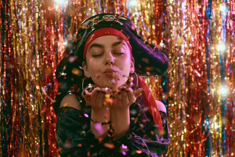Young woman in pirate costume blowing confetti in front of glittering tinsel backdrop