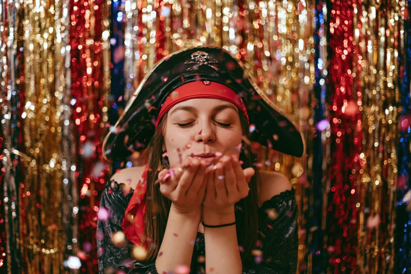 Young woman in pirate costume blowing confetti against a glittering tinsel backdrop
