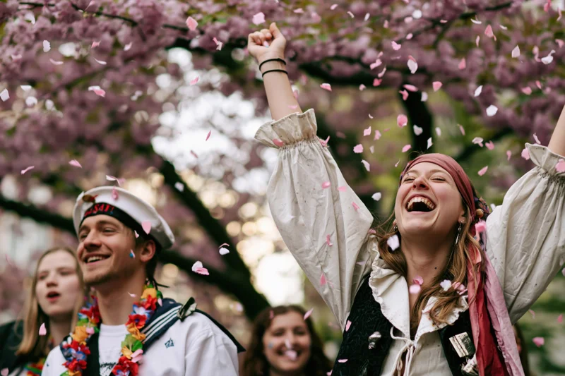 Woman in pirate costume laughing with arms raised under cherry blossoms