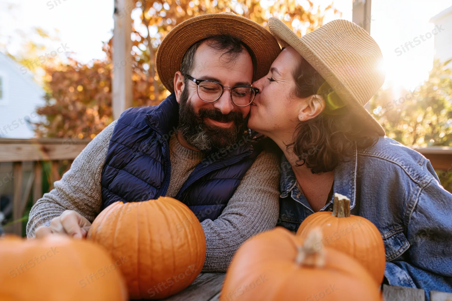 Woman kissing man on the cheek beside pumpkins on a porch