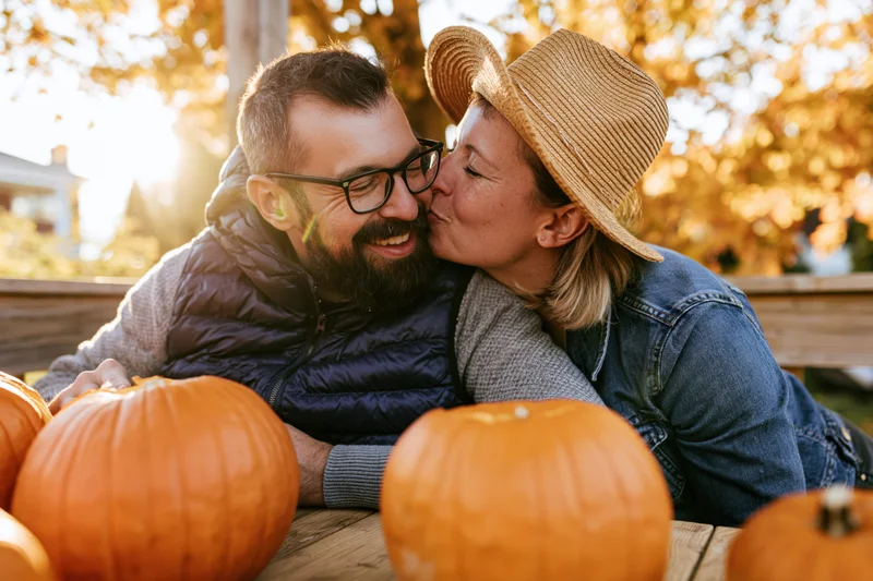 Woman kissing man on the cheek beside pumpkins in autumn garden