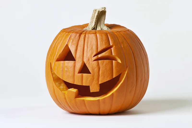 Carved pumpkin with grinning winking face on white background