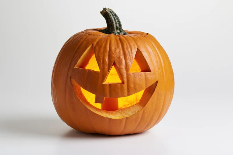 Carved pumpkin with triangular eyes and smiling mouth glowing from within on white background