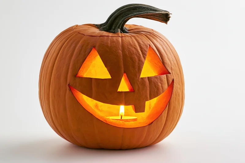 Carved pumpkin with triangular eyes and smiling mouth lit by candle on white background