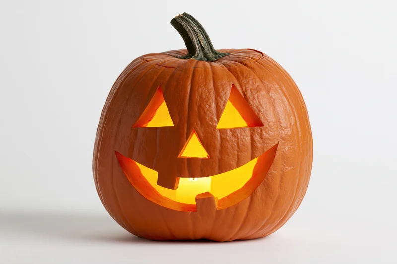 Carved pumpkin with triangular face glowing from within on white background