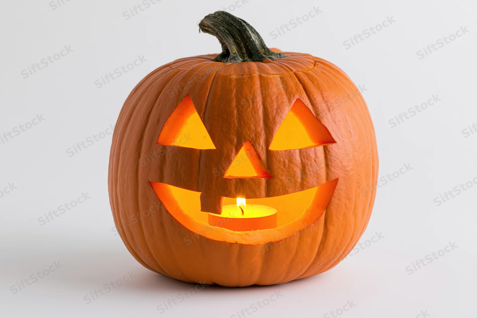 Carved pumpkin with triangular eyes and smiling mouth lit by candle on white background