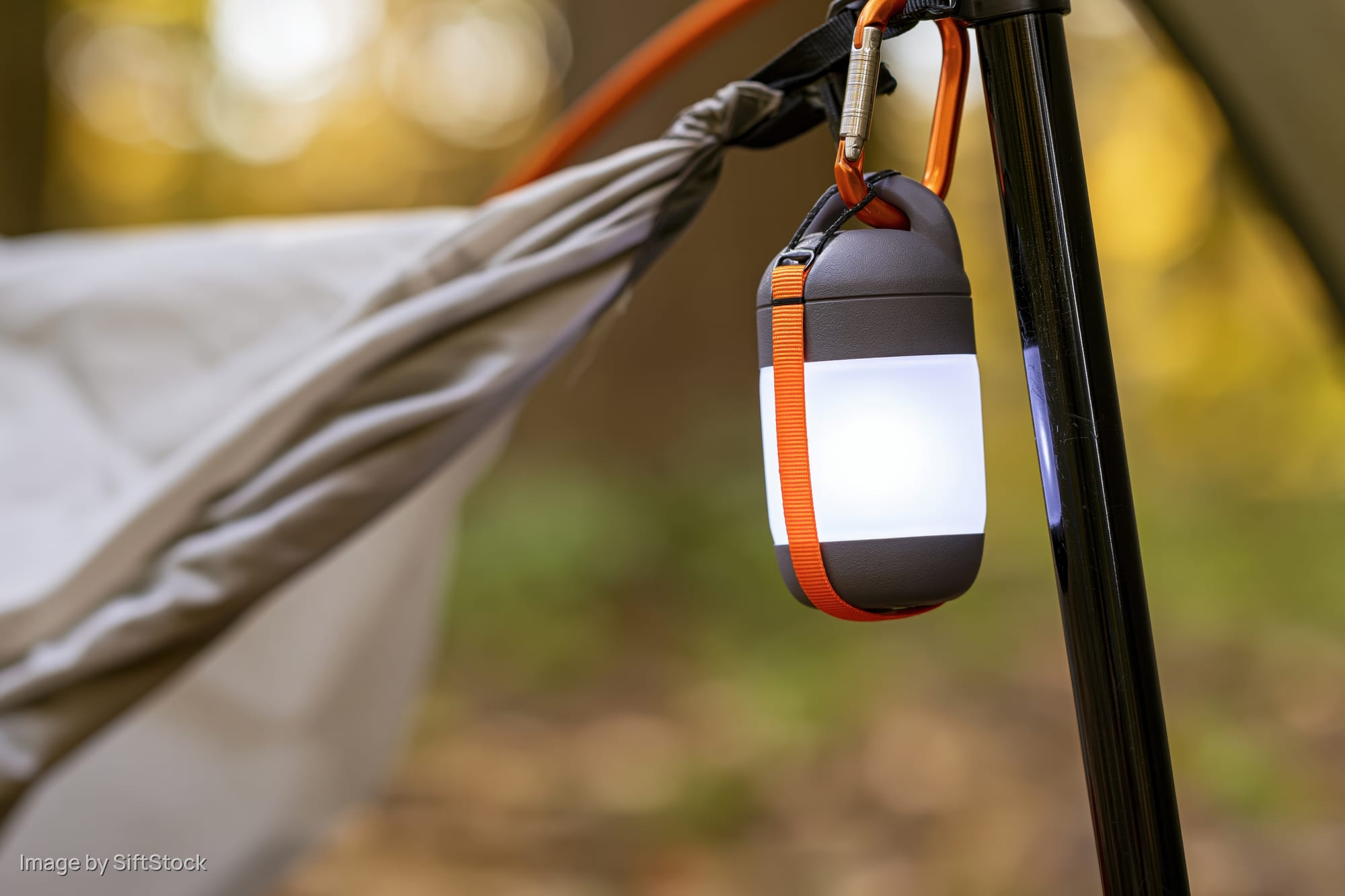 Compact led lantern glowing on tent pole in forest setting