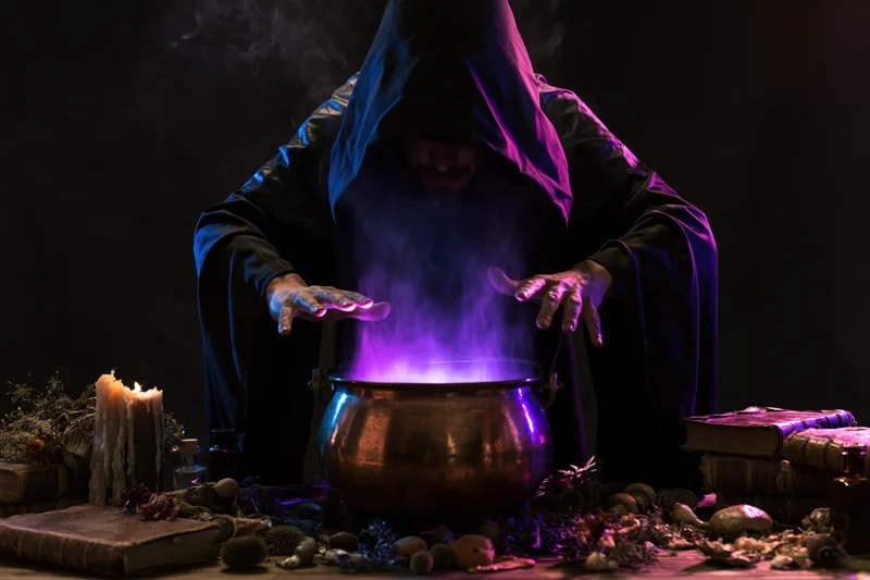 Hooded wizard casting a spell over a glowing purple cauldron on a cluttered table with books and herbs