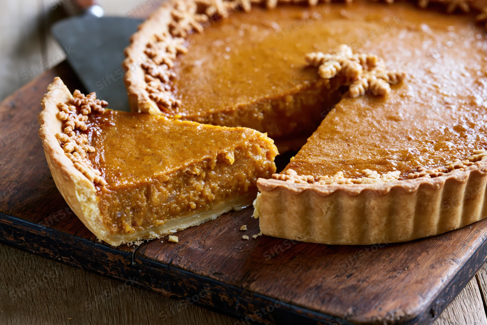 Pumpkin pie with one slice lifted on wooden cutting board