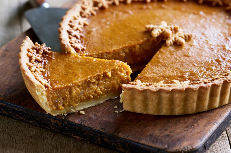 Pumpkin pie with one slice lifted on wooden cutting board