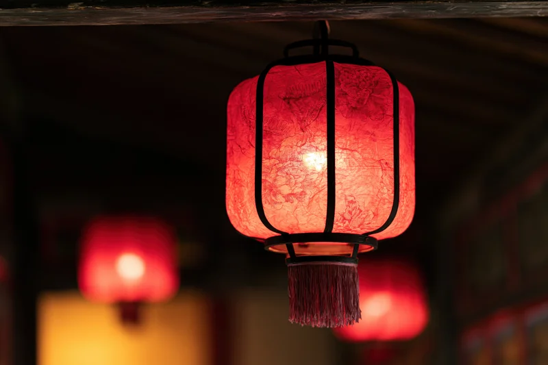 Glowing red chinese paper lantern hanging from wooden ceiling in dim interior