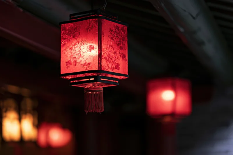 Red chinese paper lantern glowing with floral pattern hanging from wooden ceiling at night