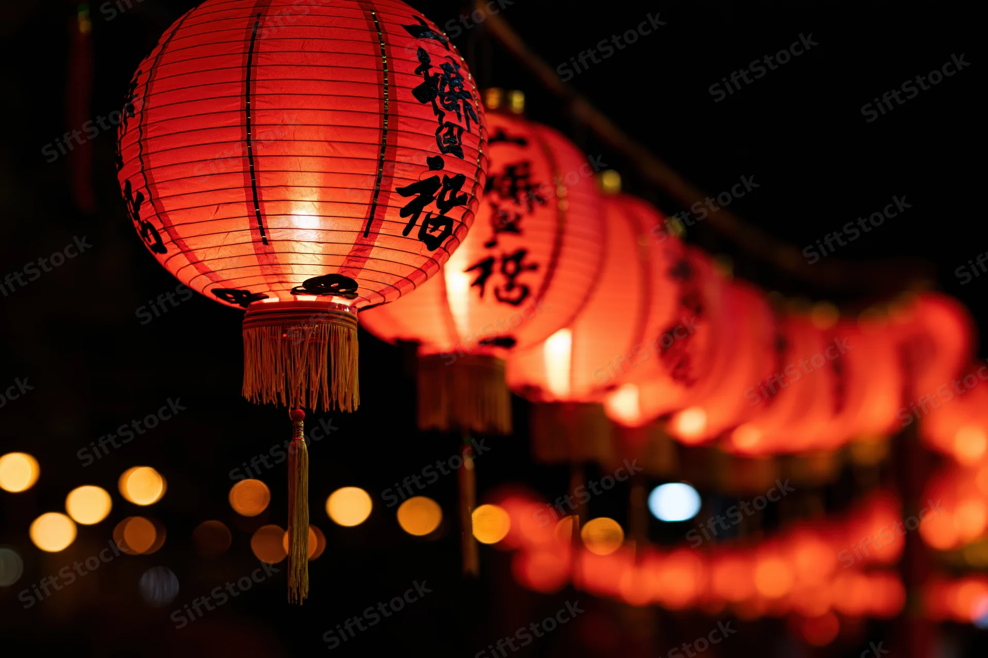 Glowing red chinese paper lantern hanging in a row at night with blurred lights in the background