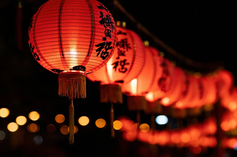 Glowing red chinese paper lantern hanging in a row at night with blurred lights in the background