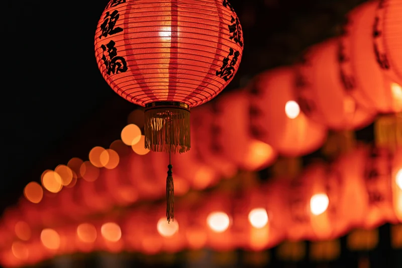 Glowing red chinese paper lantern hanging in foreground with blurred row of lanterns behind at night