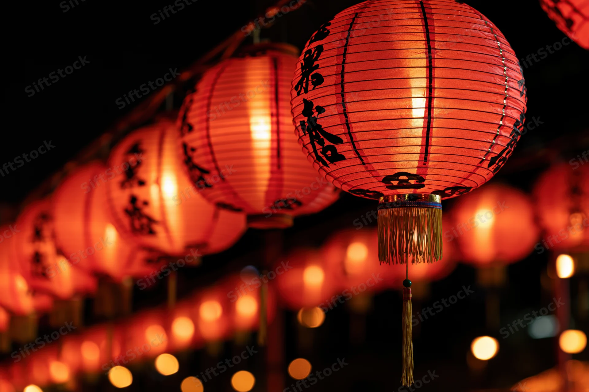 Glowing red chinese paper lanterns hanging in a row at night with calligraphy and tassels
