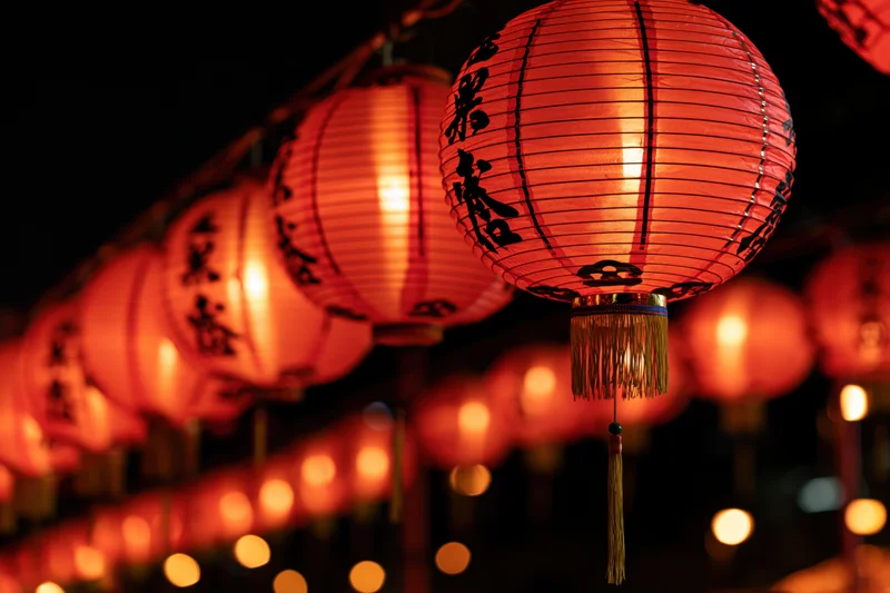 Glowing red chinese paper lanterns hanging in a row at night with calligraphy and tassels