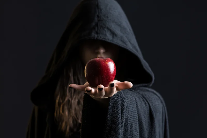 Hooded woman holding a red apple in her palm against a dark background