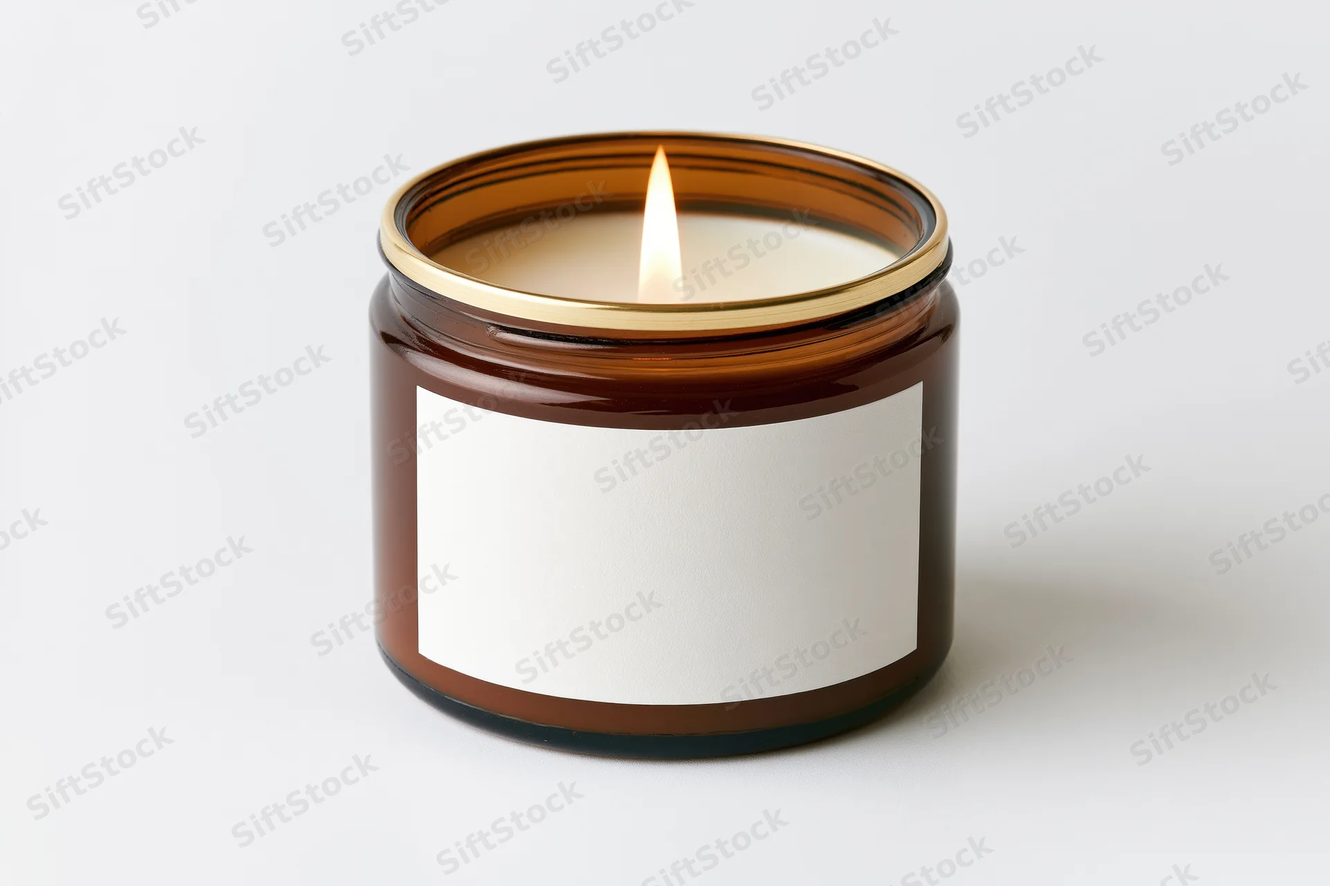 Lit scented candle in amber glass jar with blank white label on white background
