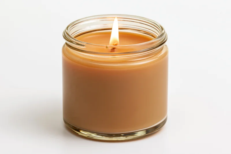 Lit soy candle in a clear glass jar glowing warmly against white background