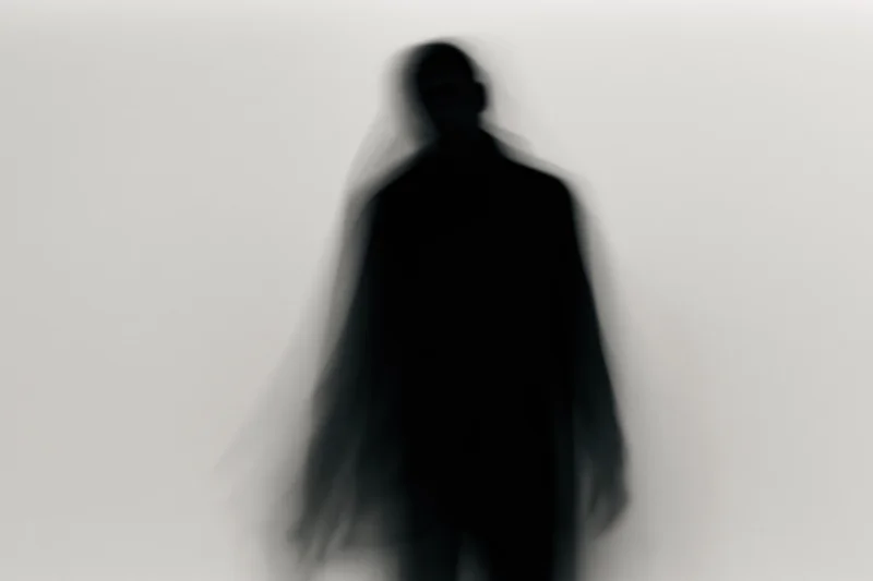 Blurred silhouette of a standing figure against a plain light background