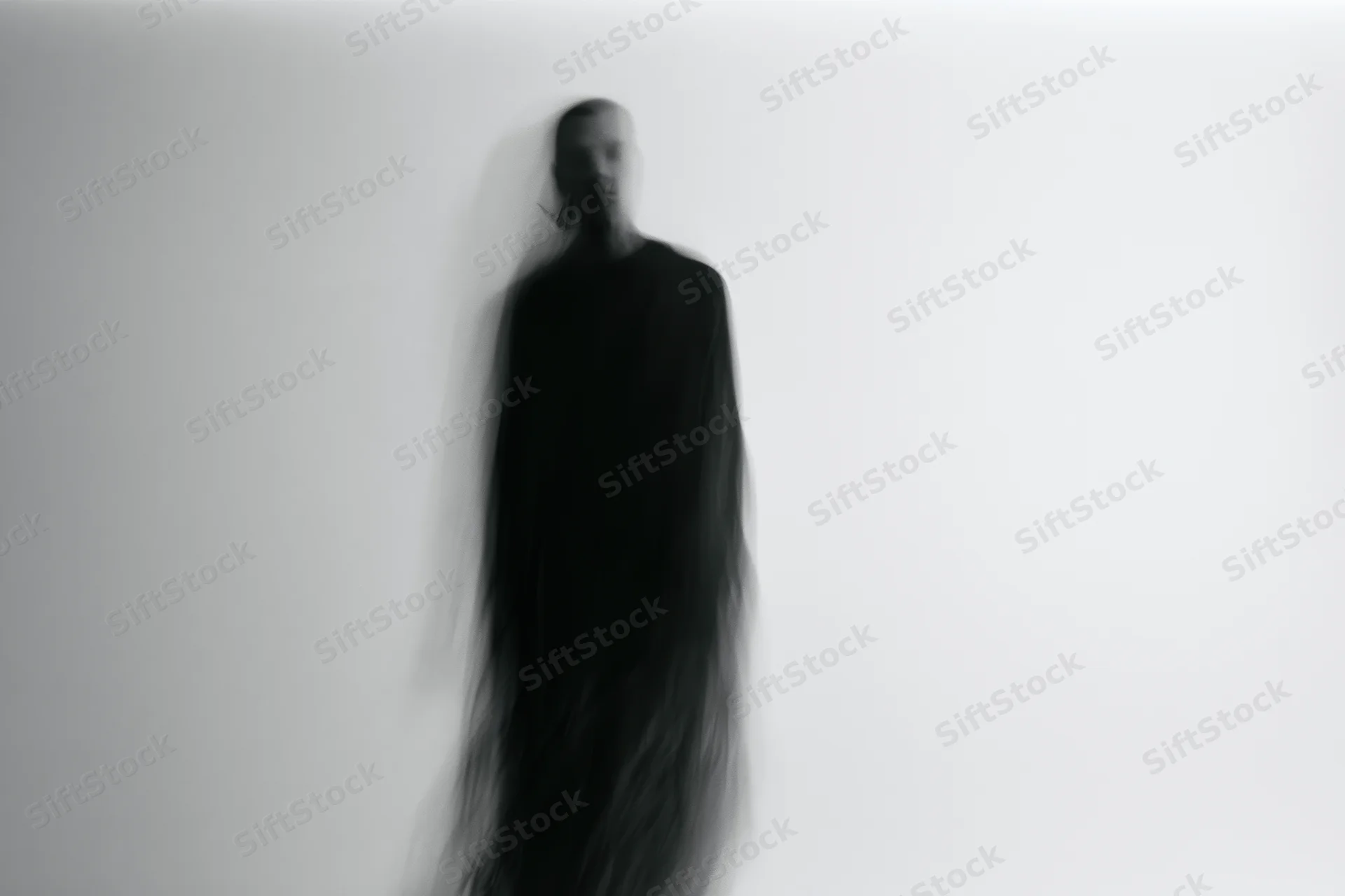Blurred silhouette of a figure standing upright against a plain light wall