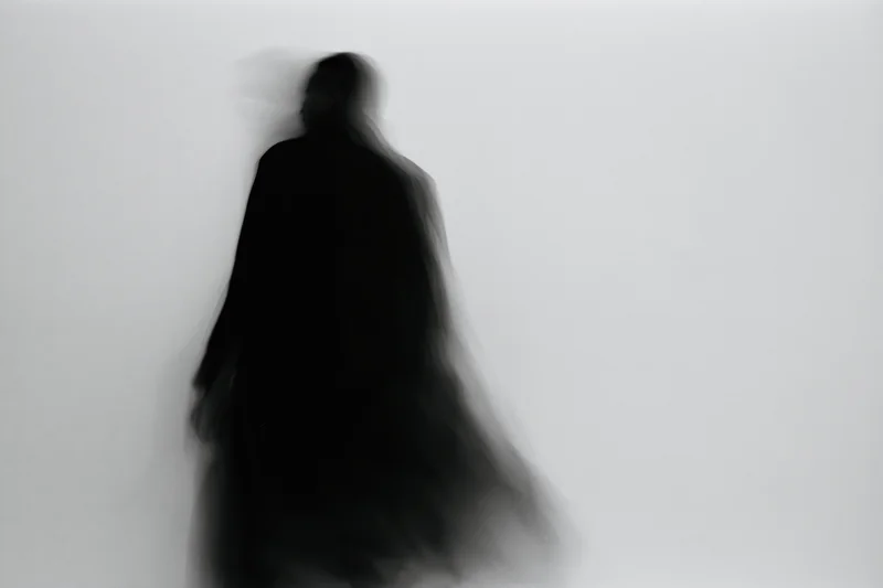 Blurred silhouette of a figure standing against a plain light background