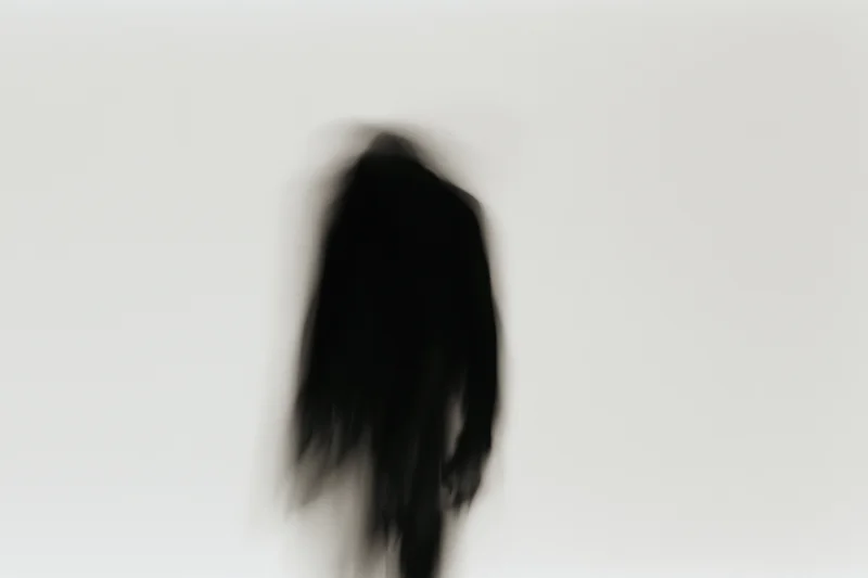 Blurred silhouette of a standing figure against a plain light background