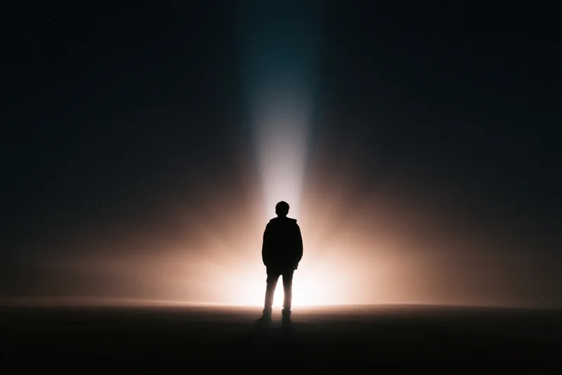 Silhouette of a person standing alone outdoors at night facing a glowing horizon under a starry sky