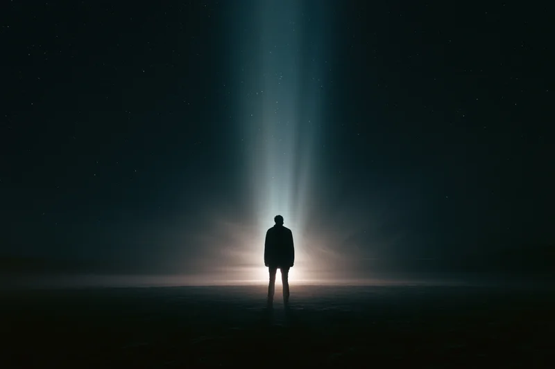 Silhouette of a person standing alone facing a glowing beam of light in a dark starry night landscape
