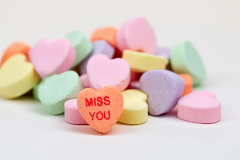 Pastel conversation hearts scattered on white surface with one reading miss you