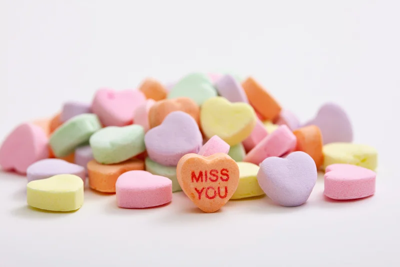 Pastel conversation hearts scattered on white surface with one reading miss you
