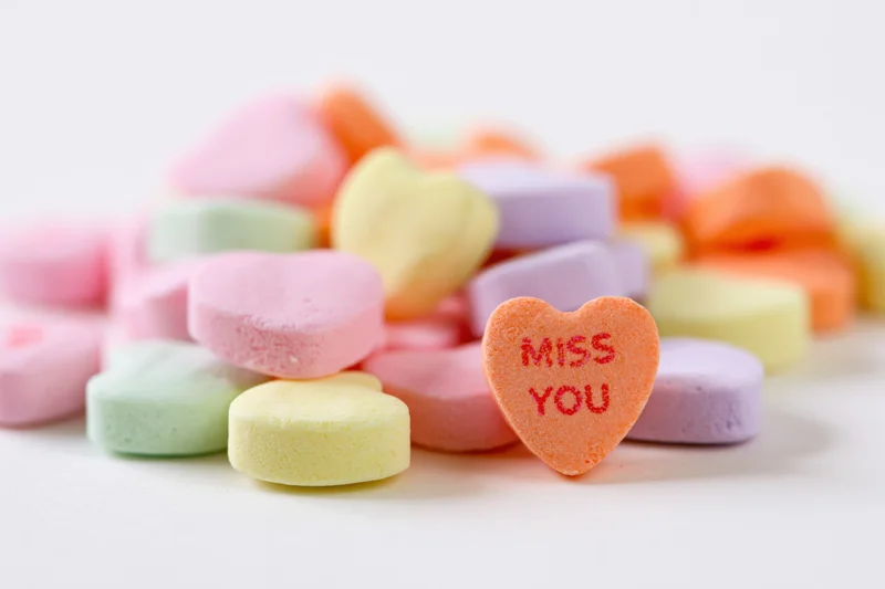 Pastel conversation hearts scattered on white surface with one reading miss you