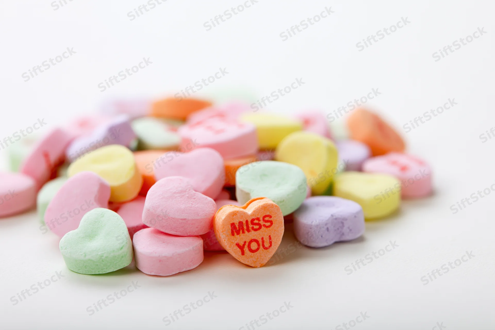 Pastel conversation hearts scattered on white surface with one reading miss you