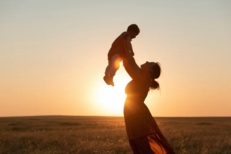 Mother lifting toddler overhead in a field at sunset