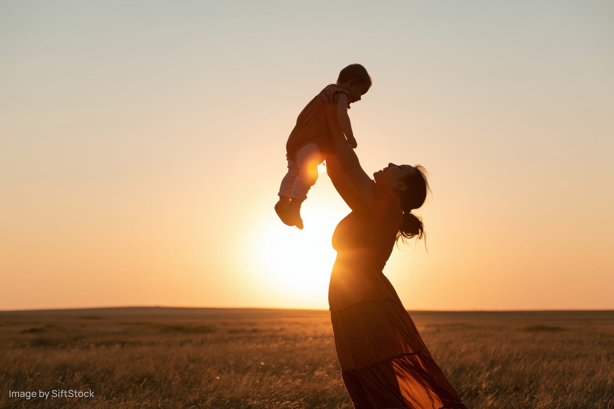 Mother lifting toddler overhead in a field at sunset