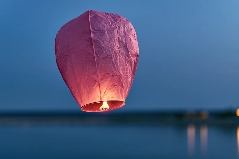 Pink paper sky lantern floating above calm water at twilight with flame glowing inside