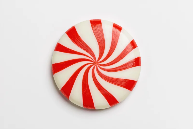Round peppermint candy disc with red and white swirls on white background