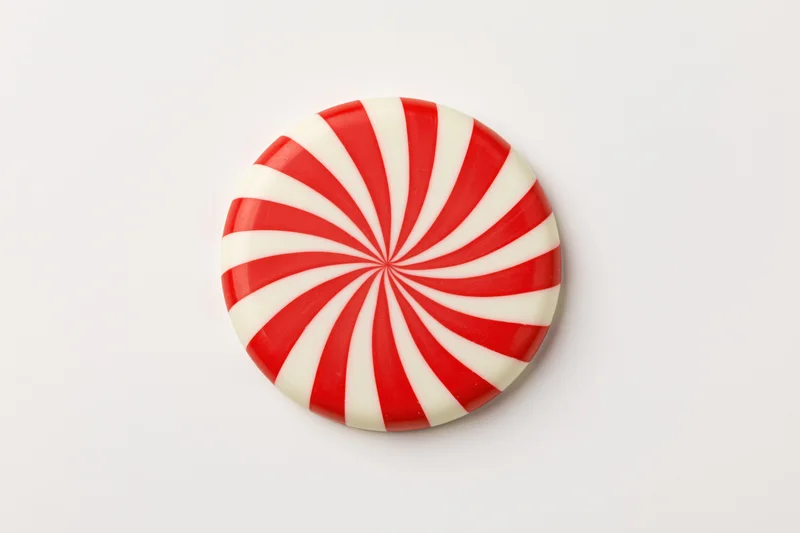 Round peppermint candy disc with red and white swirl pattern on white background