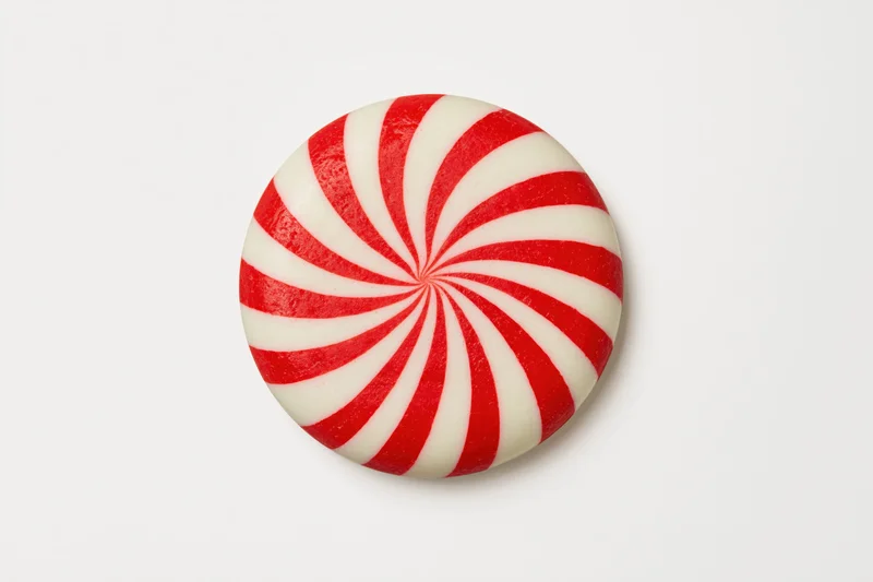 Round peppermint candy disc with red and white swirls on white background
