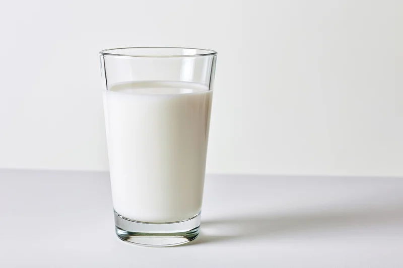 A clear glass filled with white milk on a plain white surface