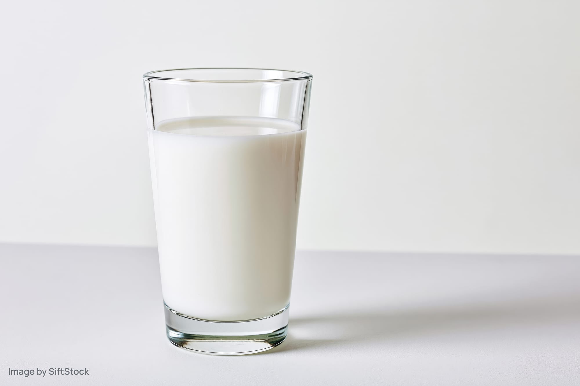 A clear glass filled with white milk on a plain white surface