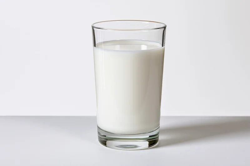 A clear glass filled with white milk on a white surface
