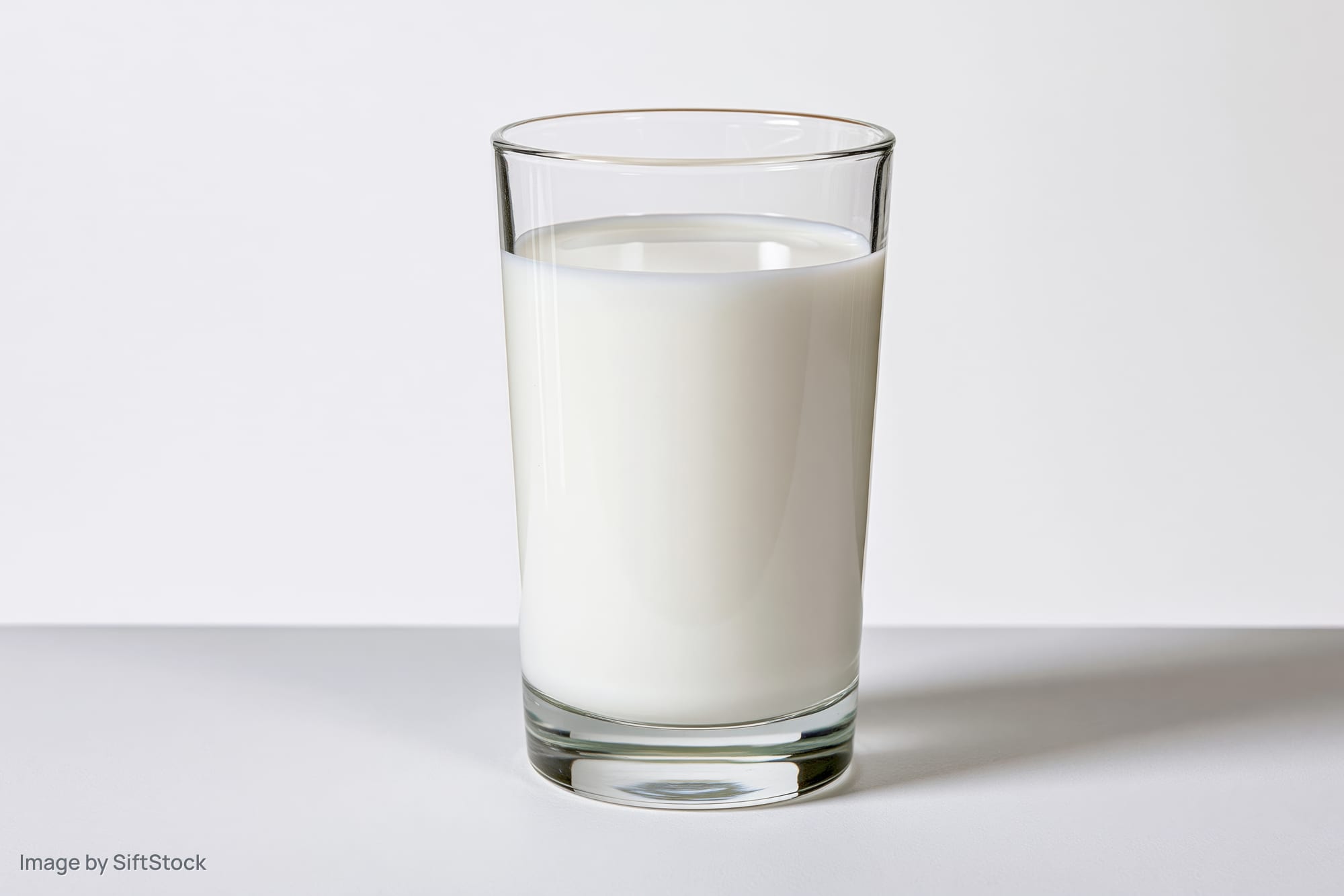 A clear glass filled with white milk on a white surface
