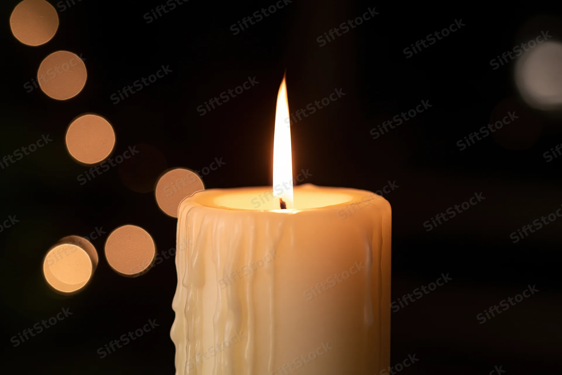 Cream pillar candle burning with a steady warm flame against a dark background with bokeh lights