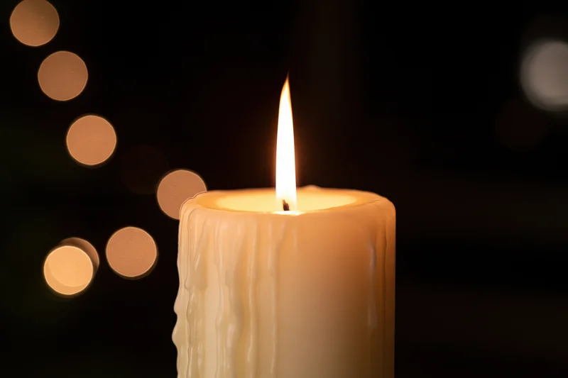 Cream pillar candle burning with a steady warm flame against a dark background with bokeh lights