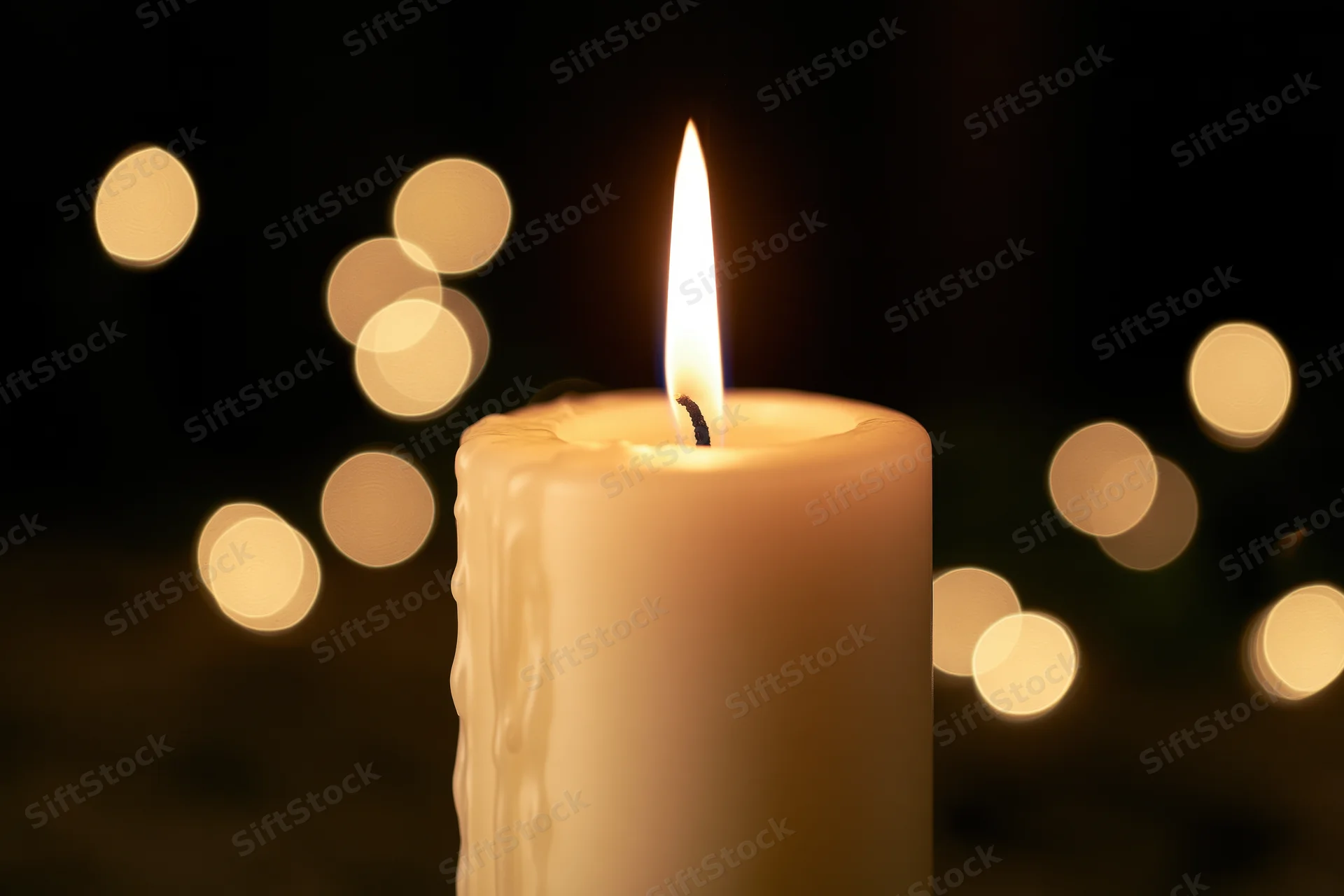 Cream pillar candle burning with steady warm flame against dark background with bokeh lights