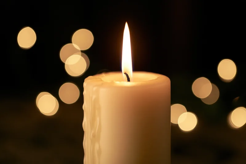 Cream pillar candle burning with steady warm flame against dark background with bokeh lights