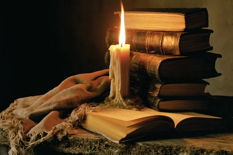 Lit candle beside a stack of old books on a stone table with burlap cloth